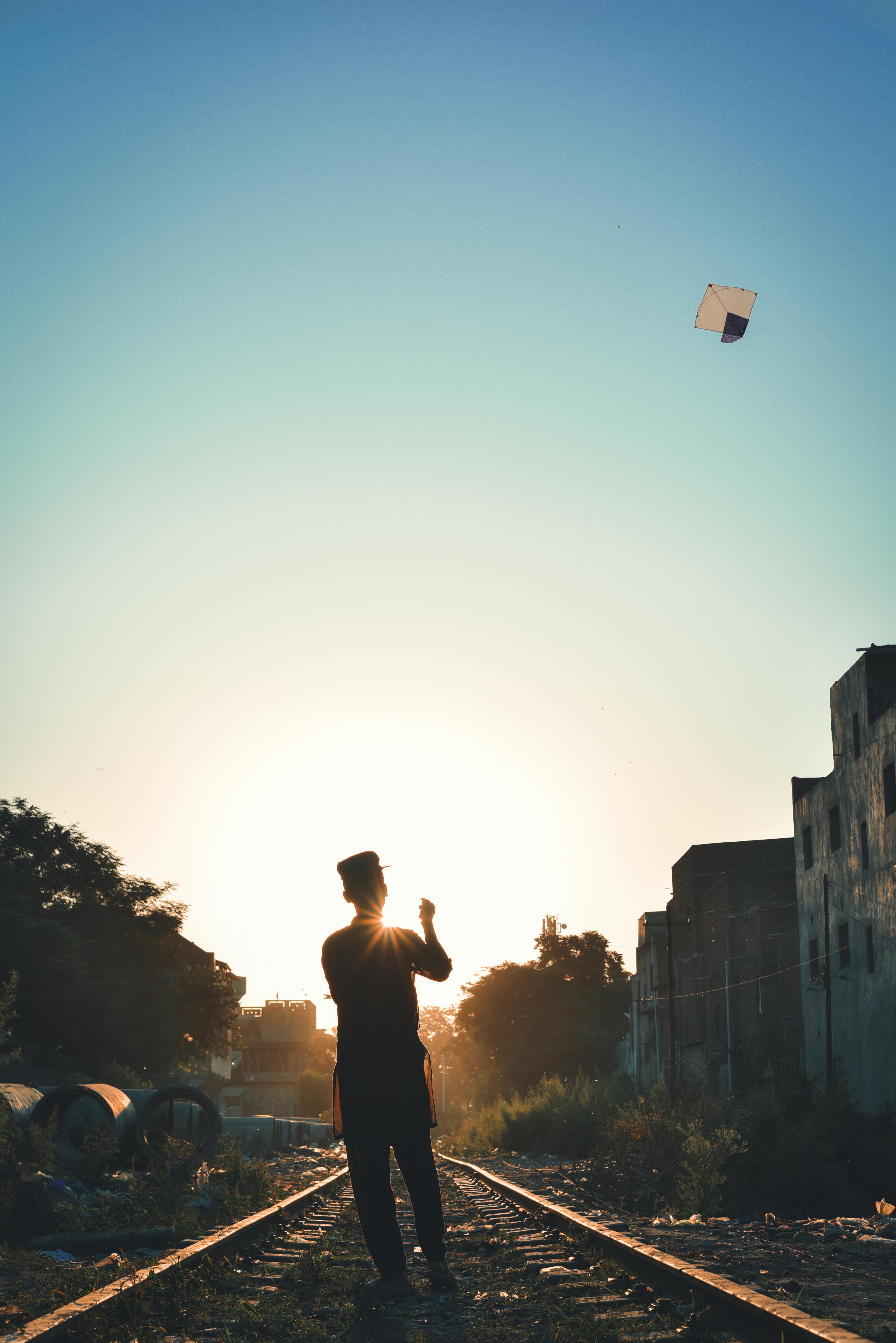 Dramatic silhouette of a person flying a kite at sunset on a railway track in Pakistan.