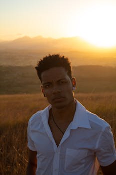 Portrait of a young man in a white shirt at sunset in a field, capturing warm, backlit atmosphere.