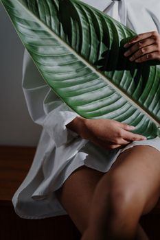 A woman in a white shirt holds a large green leaf while sitting indoors, creating a calm and natural vibe.