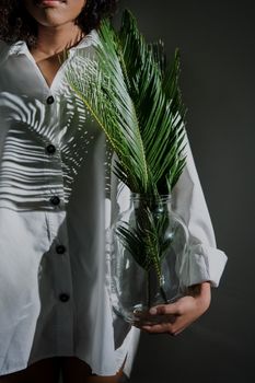 A woman in a white shirt holds a lush fern in a glass vase, showcasing natural beauty.