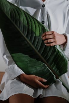 Close-up of a woman in a white shirt holding a large green leaf indoors, emphasizing nature and simplicity.