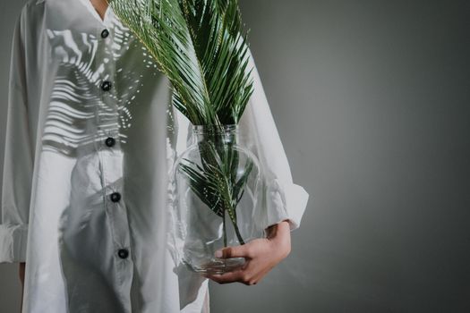 一个人拿着玻璃花瓶，里面种着郁郁葱葱的蕨类植物，在室内的白衬衫上投下艺术的阴影