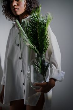一位穿着白衬衫的女人拿着一个镶有蕨类植物叶子的玻璃花瓶，光线柔和