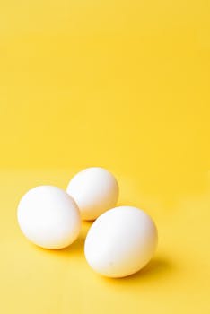 Three clean white eggs arranged on a vibrant yellow background, ideal for healthy food themes.