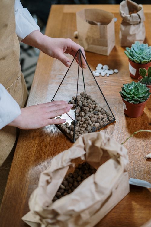 Free Close-up of hands assembling a DIY succulent terrarium with soil and pebbles in a triangular glass prism. Stock Photo