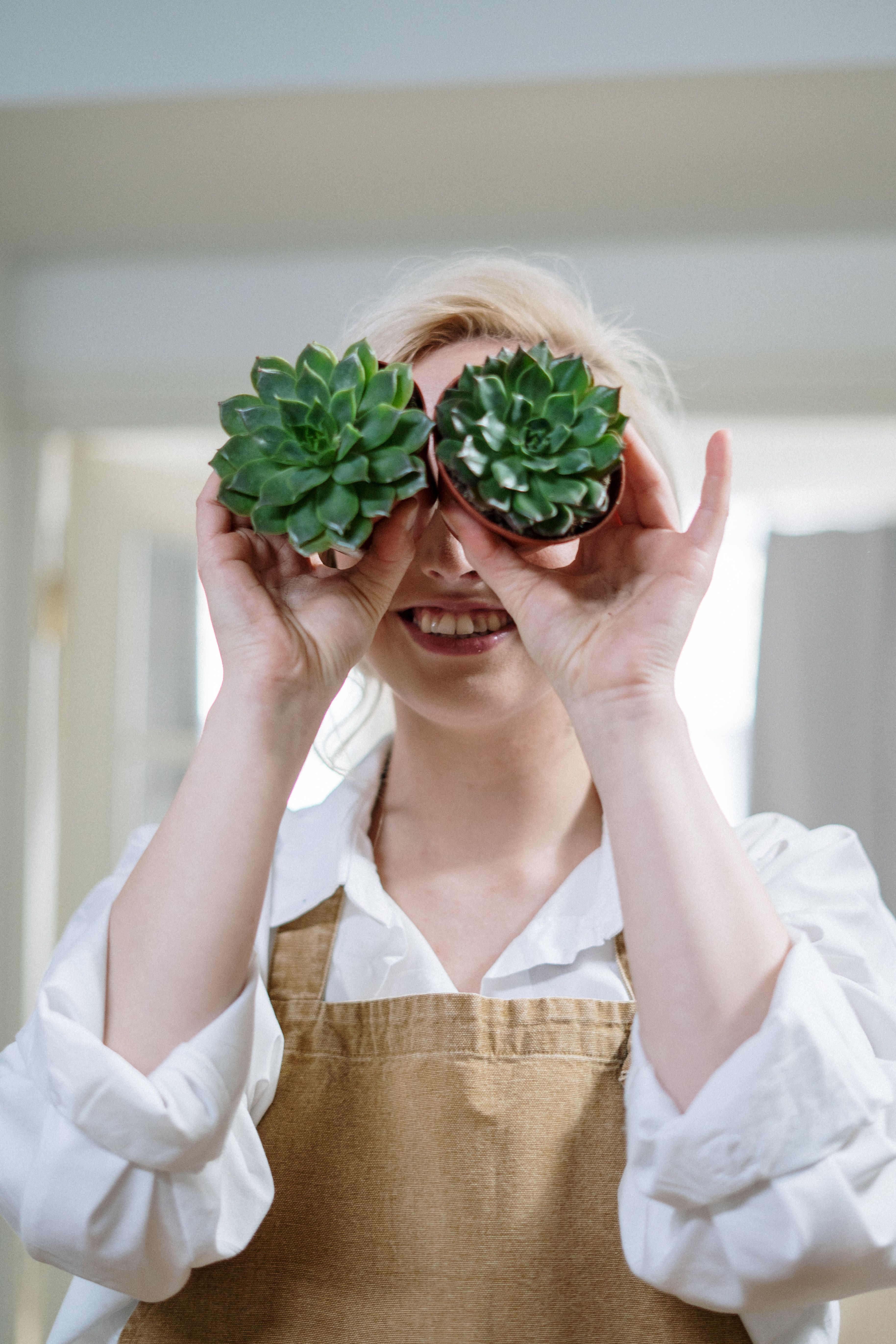 一位开朗的女人在室内拿着多肉植物当眼镜玩乐