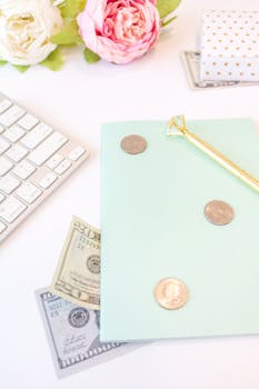 Chic flat lay featuring a notebook, pen, US dollars, and flowers on a white background.