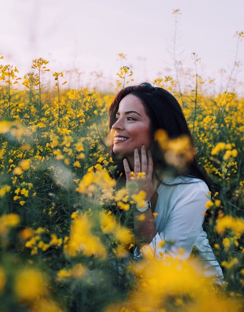 Smiling Woman in Blue Shirt Sitting on Yellow Flower Field