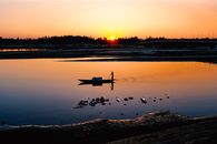 Silhouette of man floating on boat along lake in evening