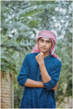 一位身穿传统蓝色服装、头戴头巾的年轻人在户外以郁郁葱葱的绿色为背景摆姿势