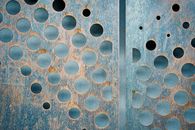 Thin rusted corrosion metal panels with carved circles of different size against gray wall