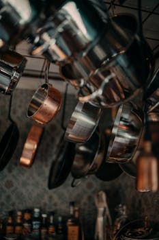 Vertical shot of stainless steel and copper pots and pans hanging in a kitchen.