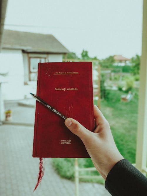 Person Holding Red Book With Black Pen