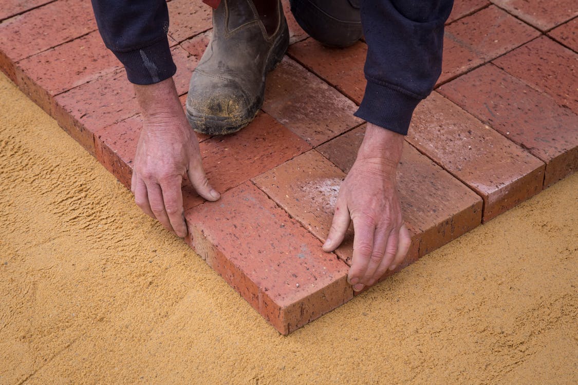 Free High angle crop anonymous worker in workwear lying bricks on sandy ground in square shape Stock Photo
