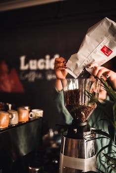 Close-up of coffee beans being poured into a grinder in a café setting.