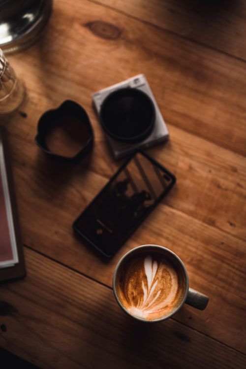 Free A warm cup of latte with art beside a smartphone on a rustic wooden surface. Stock Photo