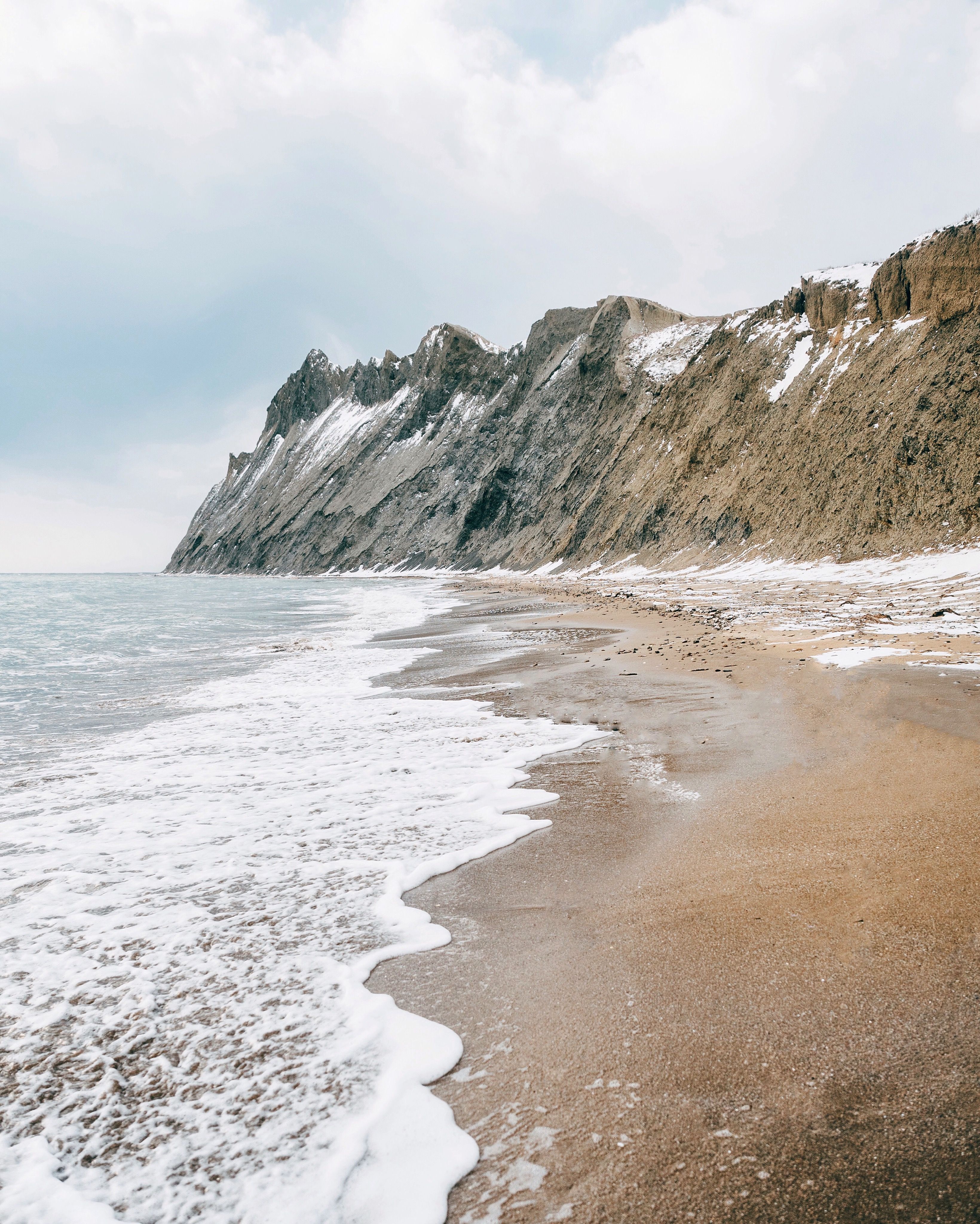 宁静的海滩上，海浪拍打着海岸，也拍打着积雪覆盖的岩石悬崖