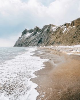宁静的海滩上，海浪拍打着海岸，也拍打着积雪覆盖的岩石悬崖