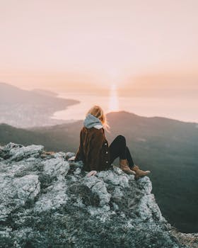 A woman sits on a rocky mountain enjoying the breathtaking sunrise view over the ocean.
