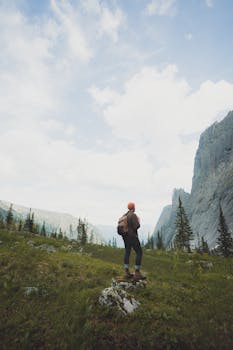 A lone hiker stands in a vast mountainous landscape, embracing nature's grandeur.
