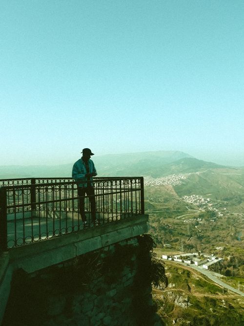 Free Unrecognizable male traveler in casual clothes and cap standing on observation deck and admiring amazing scenery of mountainous valley on sunny day Stock Photo