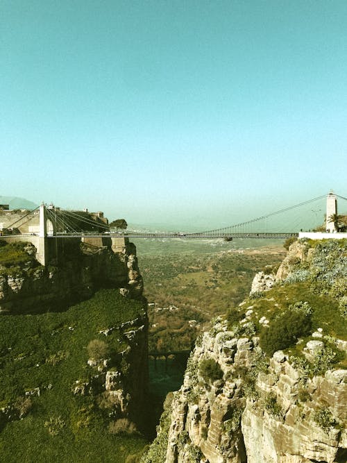 Breathtaking scenery of suspension bridge over canyon in rocky mountainous valley against blue sky on sunny day