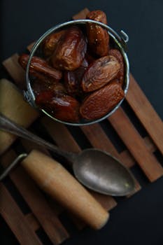 An artistic still life of dates in a small metal bucket with a wooden background.