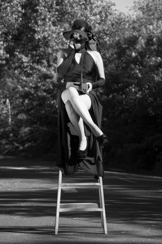 Stylish woman in black dress and hat seated on a high chair in Buenos Aires street.