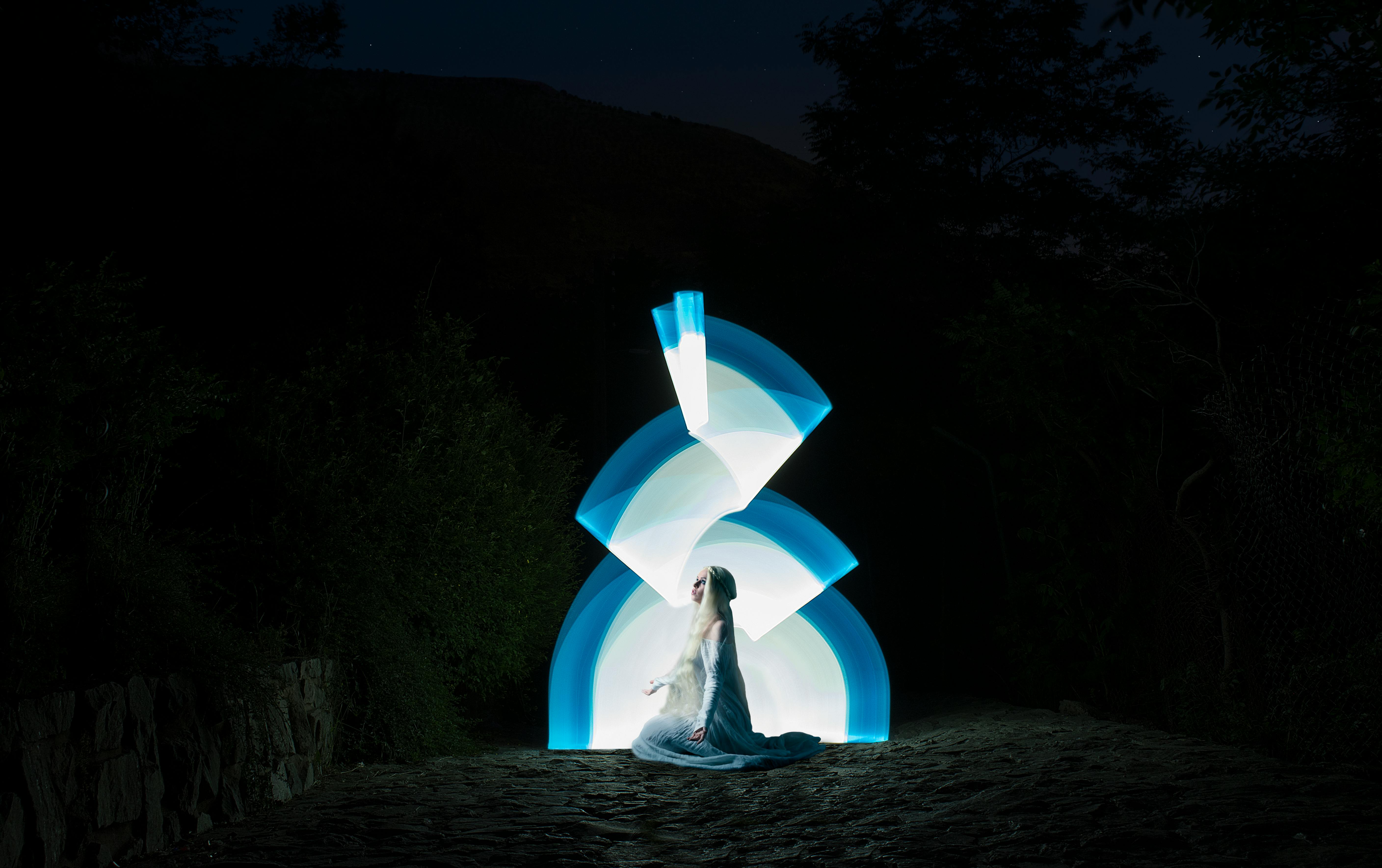 A mystical scene of a woman sitting with captivating lightpainting in a dark outdoor setting.