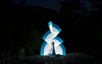 A mystical scene of a woman sitting with captivating lightpainting in a dark outdoor setting.
