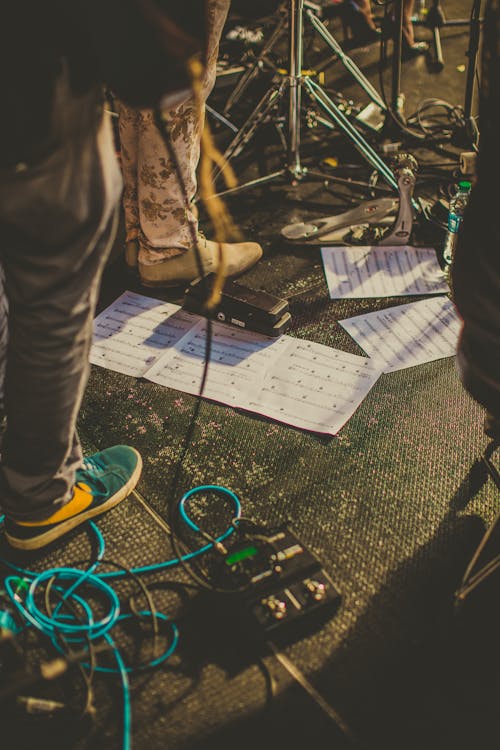 From above of crop faceless musicians standing on stage with various equipment and notes during rehearsal