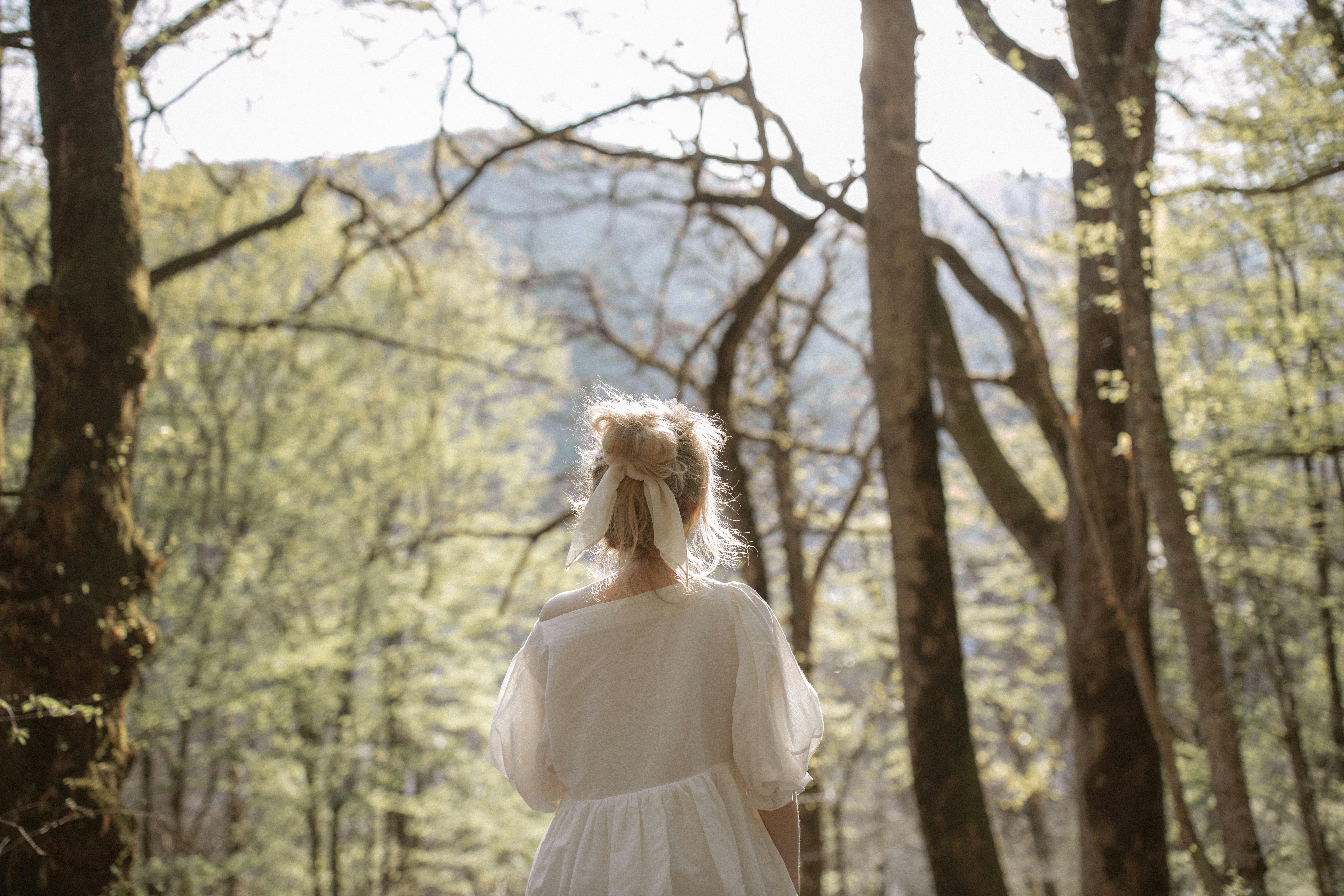 宁静的森林中，一位身穿白色连衣裙的孤独女子独自站立