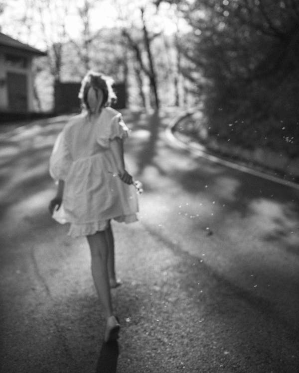 Grayscale Photo of Woman in White Dress Walking