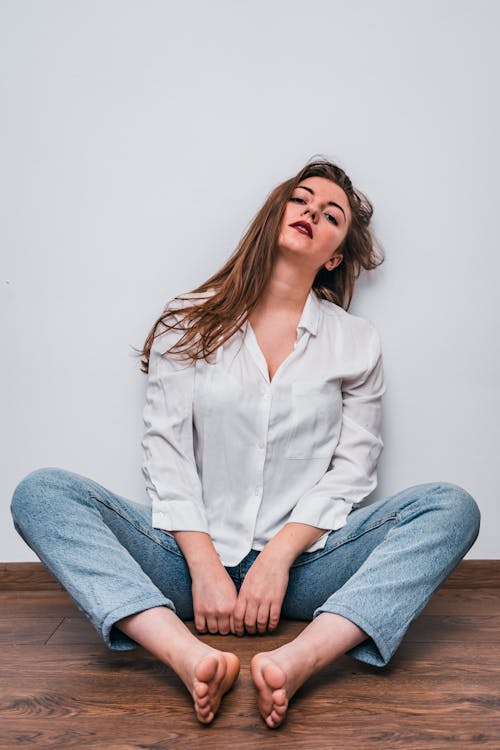 Woman in White Dress Shirt and Blue Denim Jeans Sitting on Wooden Floor