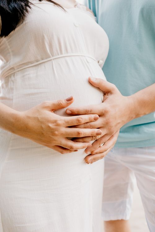Free Close-up of hands gently embracing a baby bump in a warm, serene setting. Stock Photo
