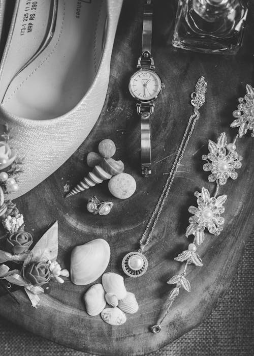 Top view of black and white elegant jewelries and shoes placed on table with various seashells and perfume bottle before wedding ceremony