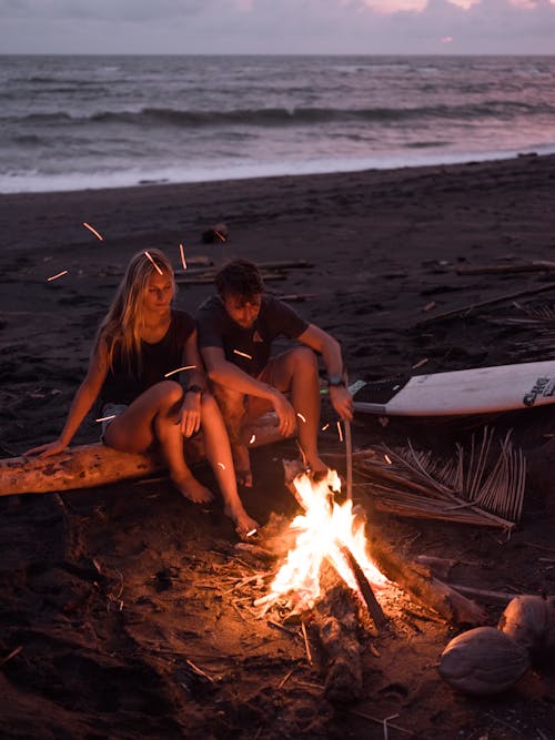 Photo of Couple Sitting on Wooden Log Near Bonfire