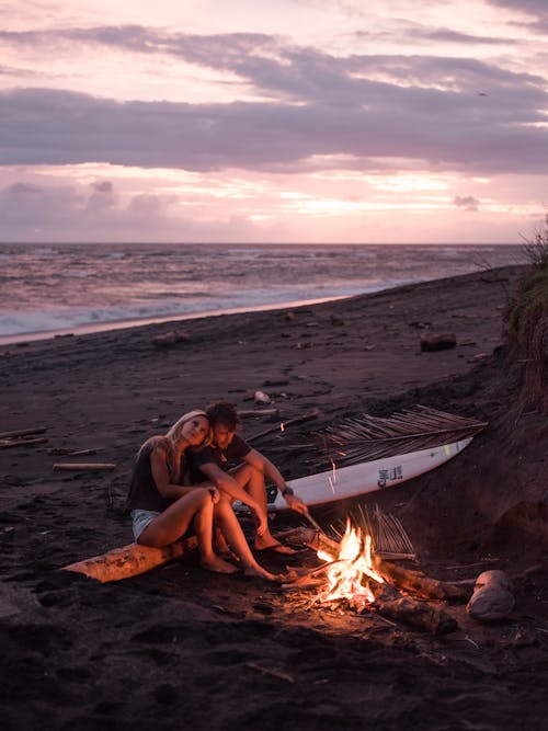 Photo of Couple Sitting on Wooden Log Near Bonfire