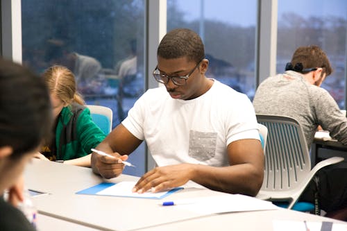 Man in White Crew Neck T-shirt Sitting on Chair While Holding White Pen