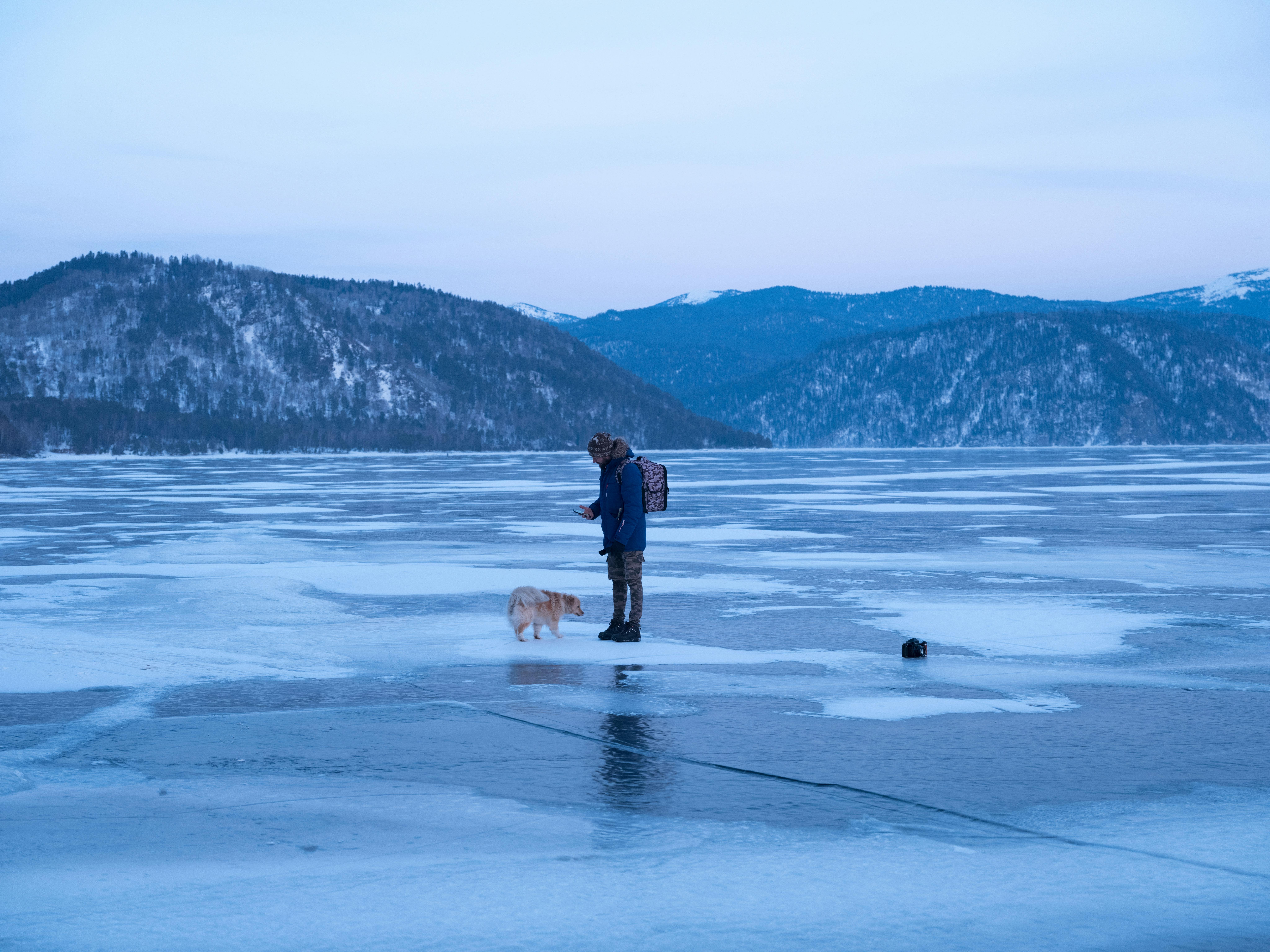 Side view of unrecognizable male in warm outerwear standing on frozen lake with cute dog during winter holidays