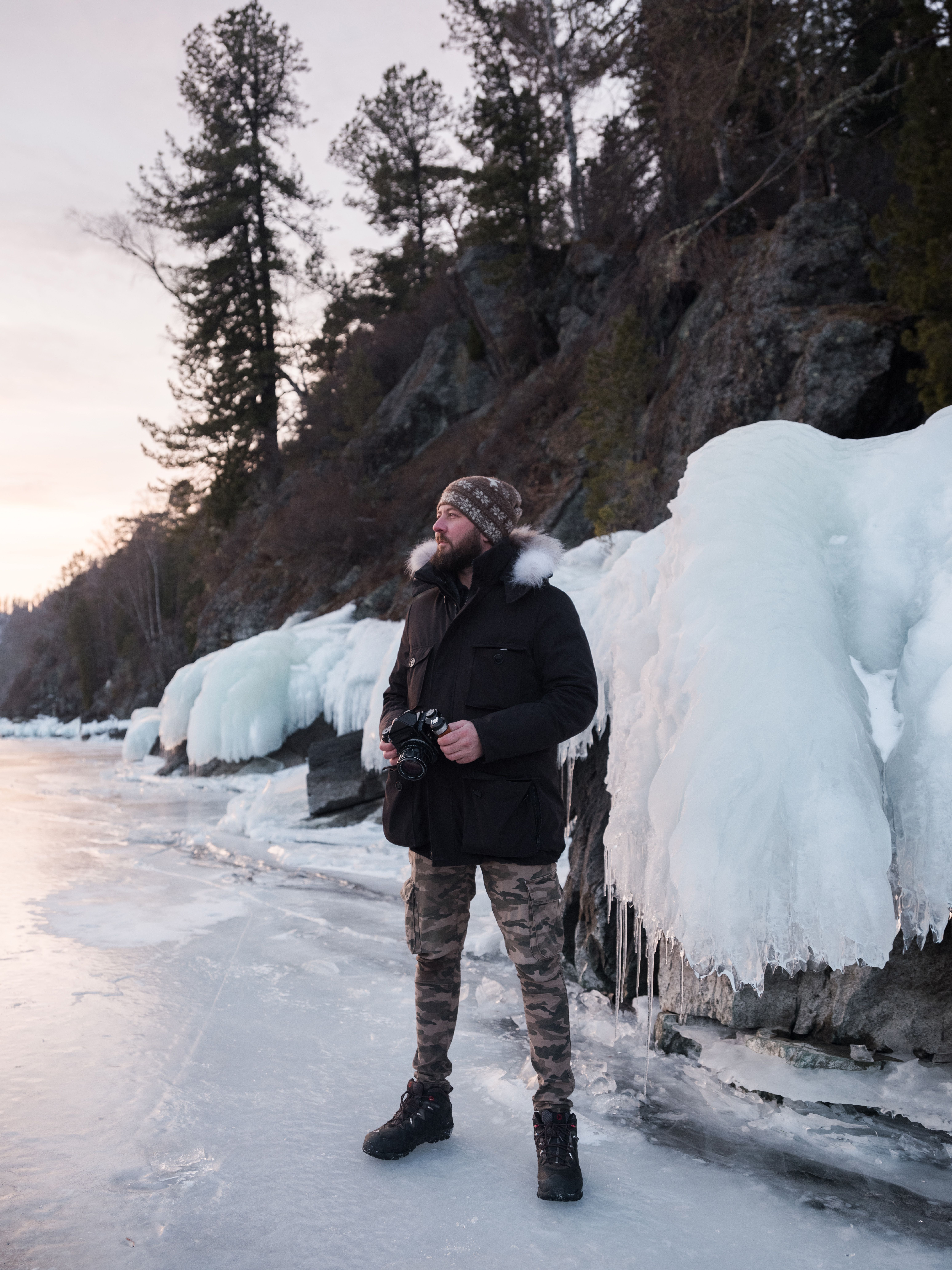 Man in winter clothing with camera on icy landscape.