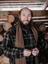 Serious senior bearded Asian male farmer in checkered shirt and scarf standing in wooden house and looking at camera