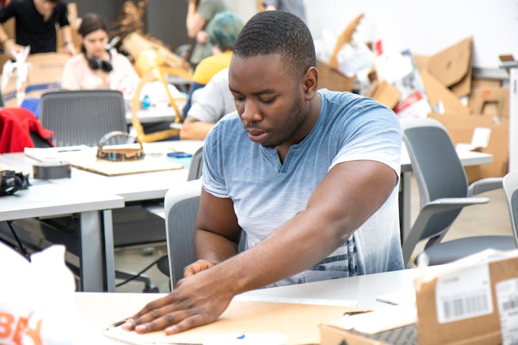 A Man In Blue Shirt Sitting Near The Table Inside The Classroom