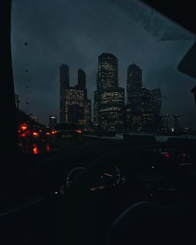 View of Moscow's illuminated skyline through car windshield at night, highlighting urban cityscape and traffic.