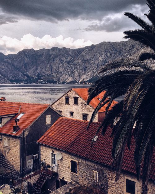 Free Old red roofed houses of village located on bay shore against mountains on overcast day Stock Photo