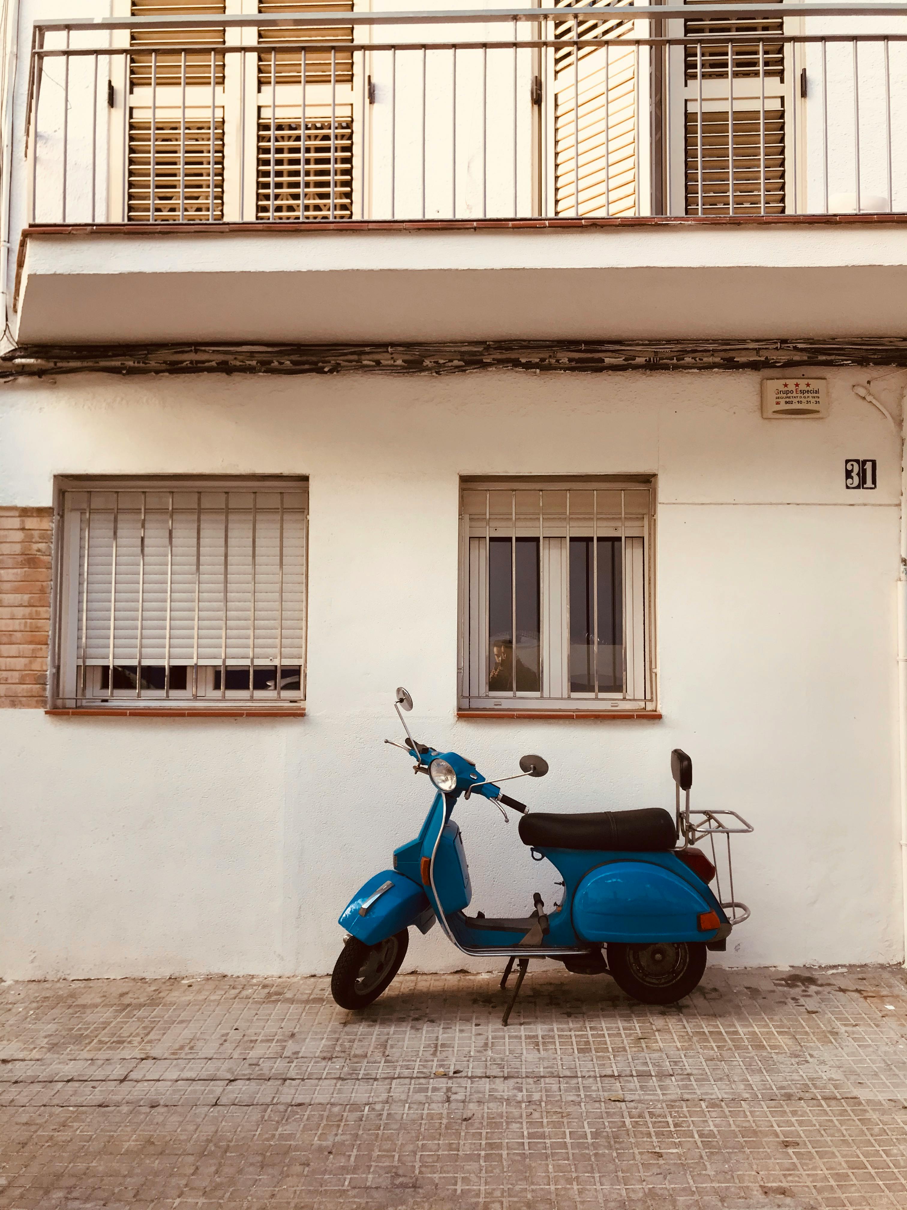 Vintage styled blue motor scooter parked on shabby pavement near white old house
