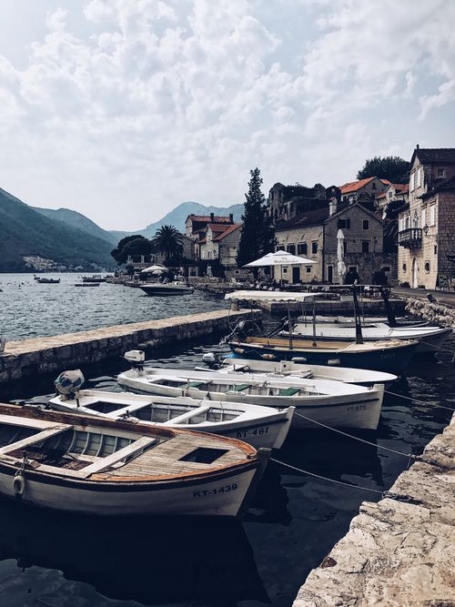 Free Traditional old fishing boats moored on shore of bay near small old houses against mountains in Perast Stock Photo