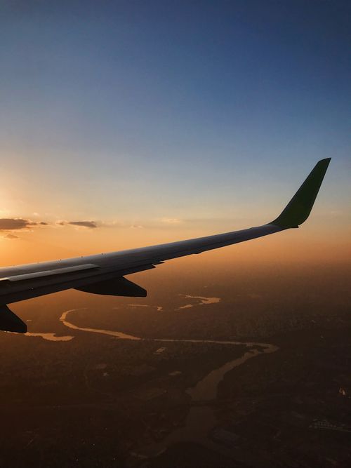 Free View of wing of airplane flying over terrain with river during beautiful sunset Stock Photo