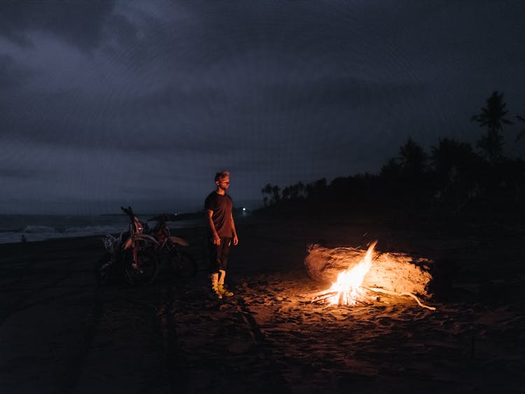 Unrecognizable Man With Burning Fire On Beach In Night