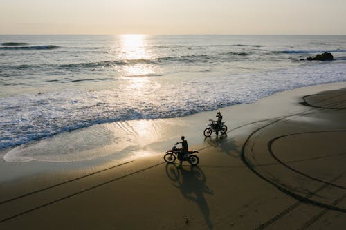 Unrecognizable bikers riding on sandy beach in sunset